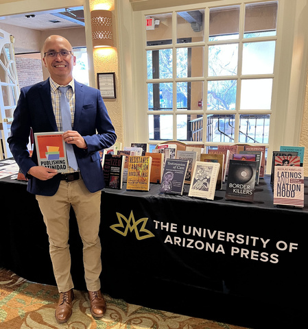 Jose Fernandez standing in front of University of Arizona Press display table holding his recent book